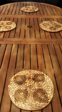 Vertical video social media - A hand preparing for an informal meal at a wooden table, by laying down raffia placemats, followed by a portable lamp.