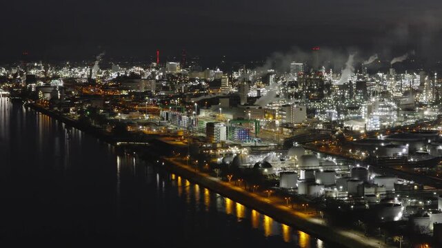 Aerial view of the massive BASF chemical plant glowing with countless lights against the dark night sky, reflecting vibrantly on the tranquil river, Ludwigshafen am Rhein, Rheinland-Pfalz, Germany.