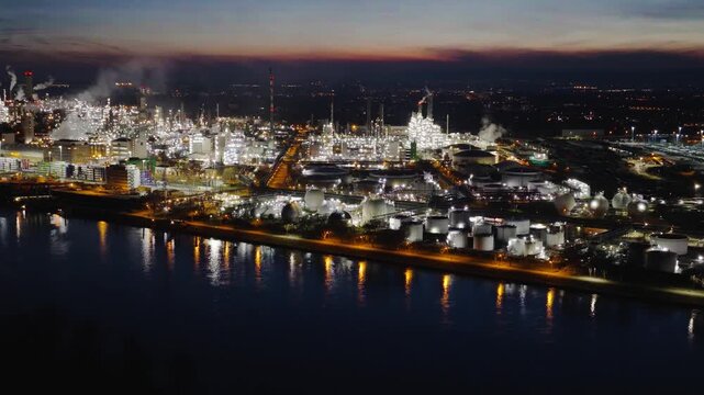 Aerial view of the sprawling BASF industrial complex glowing brightly at night, with its vivid lights reflecting on the dark river, Ludwigshafen am Rhein, Rheinland-Pfalz, Germany.