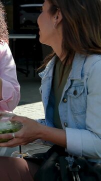 Vertical video: Reaching while friend handing salad box, woman in denim sipping juice at cafe