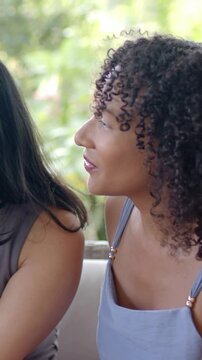 Vertical video: Hearing friend speaking, right woman leaning and smiling on porch in light blue top
