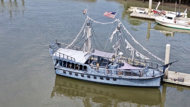 Aerial view of a striking grey pirate ship with tattered sails and an American flag docked in the murky waters, Fernandina Beach, Florida, United States.