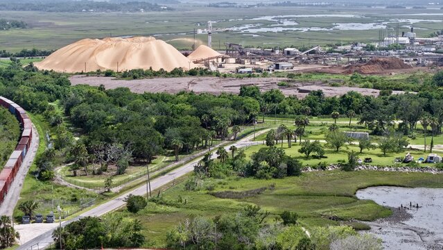 Aerial view of contrasting textures and tones between the industrial zone and the natural marshlands, with a train winding through the landscape, Fernandina Beach, Florida, United States.