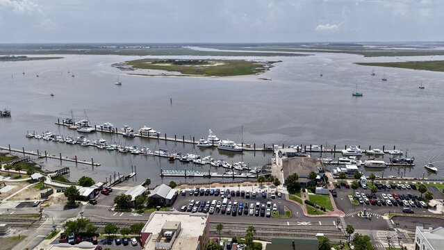 Aerial view of a bustling marina with boats on dark water, a busy parking lot, and a wide river under a hazy sky, Fernandina Beach, Florida, United States.