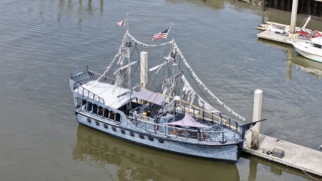 Aerial view of a whimsical pirate ship replica with tattered sails and festive bunting docked at a pier, Fernandina Beach, Florida, United States.