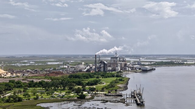 Aerial view of a sprawling industrial complex with towering smokestacks emitting plumes, contrasting with the serene marshlands and dark waters, Fernandina Beach, Florida, United States.