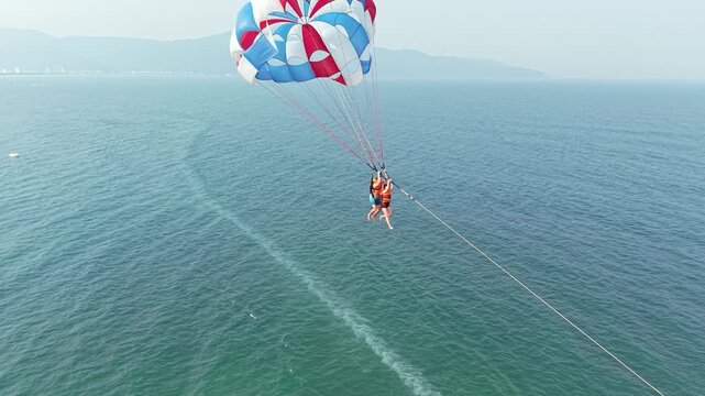 Two individuals enjoying parasailing over the blue sea during a summer vacation, experiencing adventure, freedom, and extreme water sports with a large colorful parachute