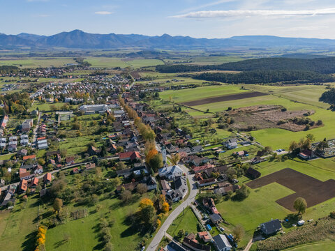Aerial view of the charming village nestled amidst vibrant green fields and distant majestic mountains under a clear sky, Klastor pod Znievom, Zilina Region, Slovakia.