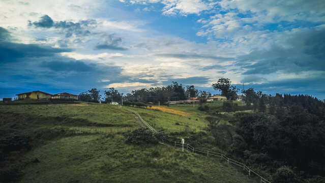Aerial view of a verdant hillside dotted with distant buildings under a dramatic, cloudy sky, Obudu, Cross River, Nigeria.