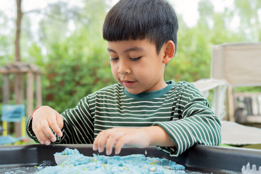 Asian cute boy playing a sandbox, using pastel-colored plastic toys to dig and build.