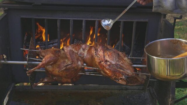 Chef basting roasting lamb and turkey on a rotisserie spit