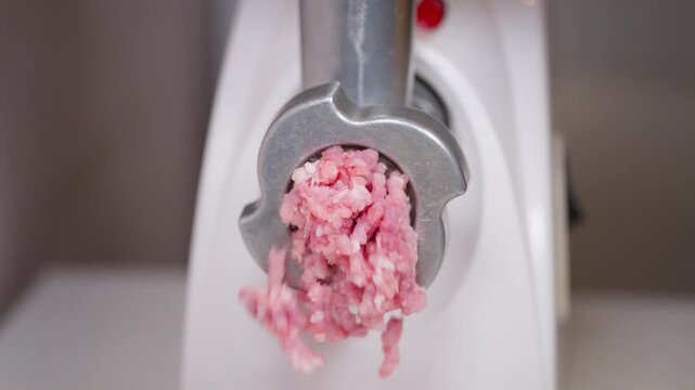 Meat grinding scene. Close view of meat extruding from electric grinder with textured pork. Detailed image showing raw minced pork emerging from meat grinder against white surface