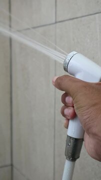 Close up hand pressing bidet sprayer trigger in bathroom hygiene routine