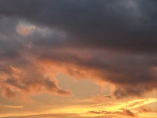 Fototapeta premium Dramatic sunset sky with glowing orange clouds and dark storm formations creating moody atmospheric background