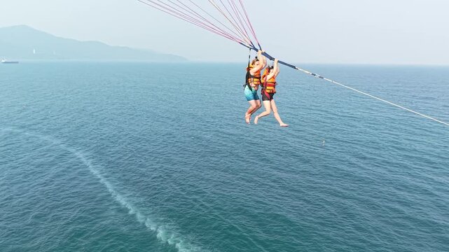 People parasailing high above the vast blue ocean, experiencing thrilling airborne adventure and freedom during a tropical summer vacation, enjoying an exciting water sport