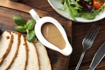 Naklejka premium Tasty turkey gravy in sauce boat, baked meat and salad on wooden table, flat lay
