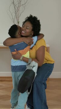 Vertical video: Opening front door, mom in mustard top carrying gray bag greeting son at home entry