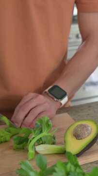 Vertical video: Arranging celery then chopping on board for meal, man in kitchen orange tee knife