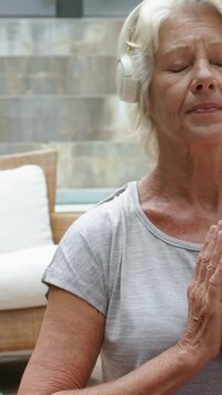Vertical video: Pulling back showing senior in grey tee praying on patio for meditation, headset