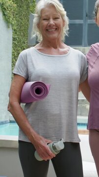 Vertical video: Approaching, woman in mauve top embracing friend and posing poolside with mats