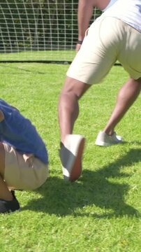 Vertical video: Father and son after tumble pushing up in backyard, son in blue tee near goal, ball