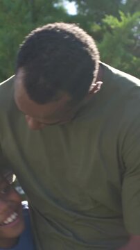 Vertical video: Leaning father hugging child in park, bonding with olive green tee and blue shirt