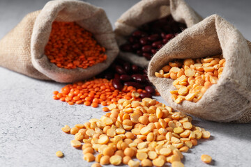 Fototapeta premium Burlap bags with different beans and legumes on light grey table, closeup