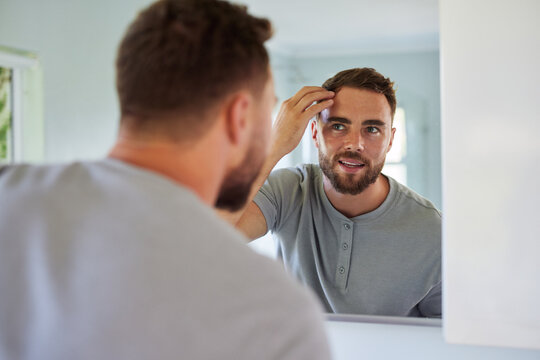 Man adjusting and checking hair in bathroom mirror