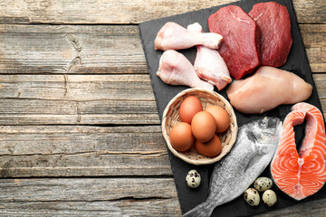 Naklejka premium Different types of fresh raw meat, fish and eggs on wooden table, top view. Space for text