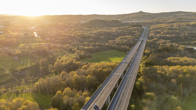 Aerial view of the Viaducto Arnoia spanning a lush green valley with cars driving during a golden sunset in Allariz, Province of Ourense, Spain.
