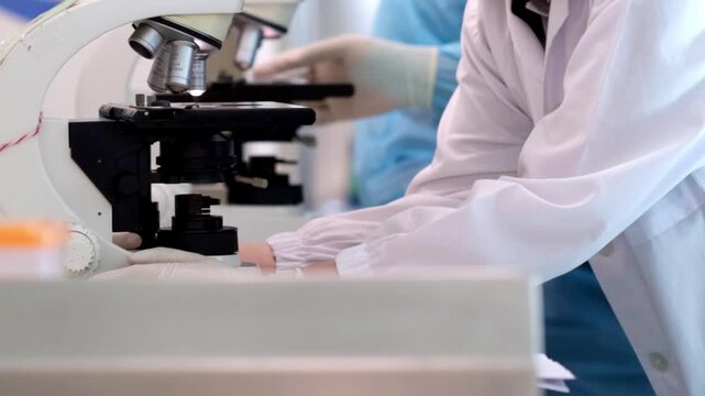 Microscope in laboratory with gloved technician in blue protective gown medical research and scientific analysis of sterile clinic sample work inside laboratory equipment