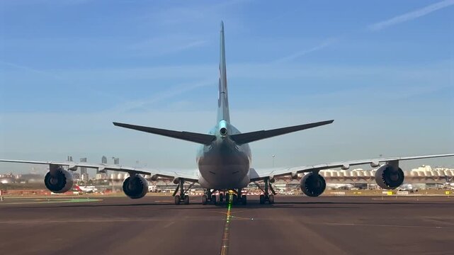 Closeup view of the rear fuselage of a massive 747 wide-body jet taxiing through Madrid airport, illuminated by the sunset light, with ther Terminal 4 and Madrid skyline at the background.