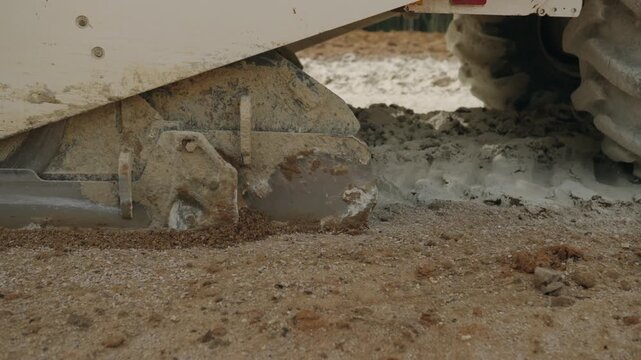 Slow motion close-up of a road construction machine churning wet gravel and slurry during ground stabilization on a worksite.