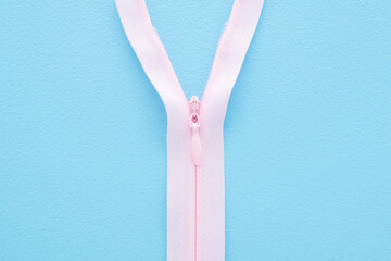 Opened new pink invisible zipper for clothes on light blue table background. Pastel color. Closeup. Top down view. © fotoduets