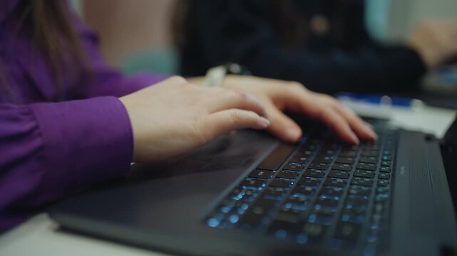 Close-up shot of a person using a laptop keyboard and trackpad while working at a desk in an office environment.