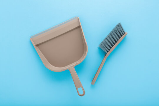 New brown broom and dustpan for home floor sweeping on light blue table background. Pastel color. Closeup. Top down view.