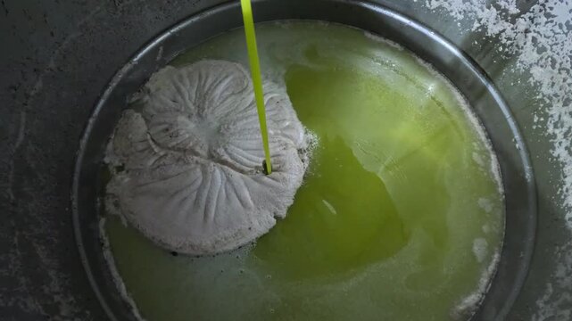 Fresh, cold-pressed olive oil flowing into a large container during the extraction process, showing a golden liquid with natural foam pul, highlighting traditional and industrial olive oil production.