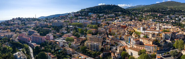 Fototapeta premium Aerial view of Grasse, France, shows pastel terraces, Cathedral Notre Dame du Puy bell tower, medieval lanes, modern blocks, midday light, clear skies, long shadows.