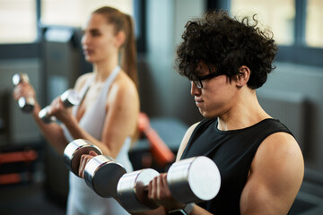 Fototapeta premium Young adult women lifting dumbbells during strength training session in gym, building fitness and healthy lifestyle concept. Ideal for wellness marketing, sports ads, personal training
