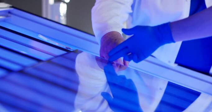 Two technicians in white lab coats and blue gloves inspecting a large transparent glass panel on a production table