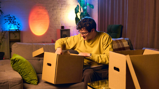 Man looking inside opened package box in warm home interior with ambient lighting. Concept of order fulfillment, product inspection, and online shopping delivery process.
