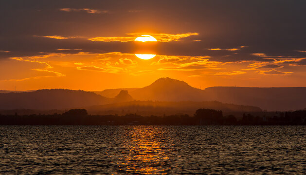 A serene sunset over Lake Constance (Bodensee) with warm golden and orange tones reflecting on the water. 