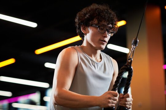 Teenage Caucasian boy exercising with cable machine in gym, building strength and healthy routine. Useful for fitness marketing, youth wellness campaigns, sports training content