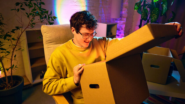 Man opening large cardboard box with surprise and smile in cozy interior. Concept of online shopping delivery, ecommerce experience, unboxing moment and customer excitement.