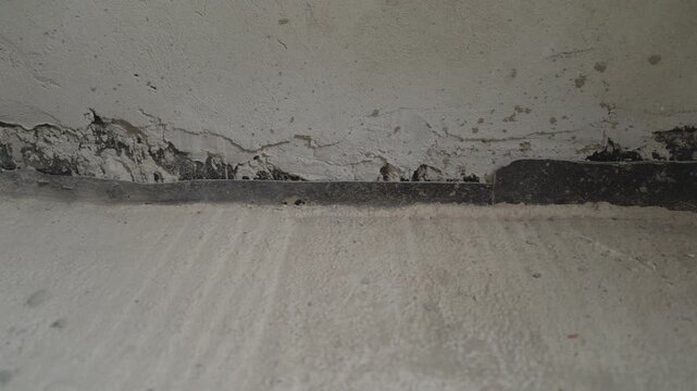 Close up panning shot revealing a crumbling and peeling plaster wall. Shows signs of damp, water damage, and potential black mold growth at a construction joint. Concept of building decay and repair