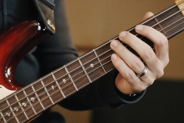 Fototapeta premium Man plays five string bass guitar, fretting notes on fretboard. Close up of hand on instrument strings, musician practicing. Focus on fingers, wood neck, and steel strings.