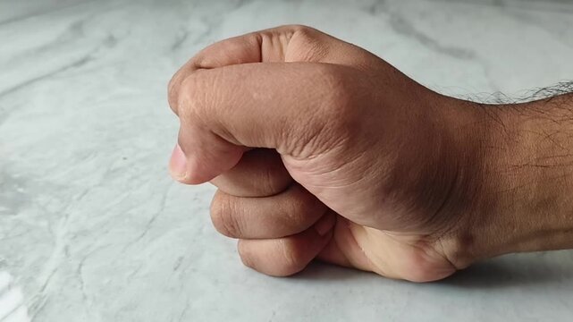 Angry asian or indian fist pounding a wall. A person is upset and forms a fist to hot the wall in a fit of madness and frustration. Closeup top view.