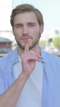 Outdoor Portrait of Young Man with Finger on Lips, Please be Quiet, Vertical Video