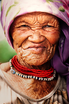 portrait of an Elderly San Woman with deep wrinkles in Rural Botswana, wearing traditional orange and white beaded necklaces
