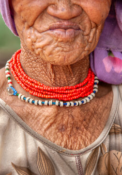 Detailed close up of elderly San Basarwa woman showing wrinkled skin and traditional orange and white beaded necklaces in rural Botswana Africa.